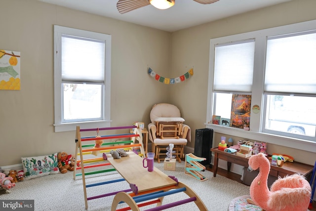 recreation room with ceiling fan, radiator, carpet, and plenty of natural light