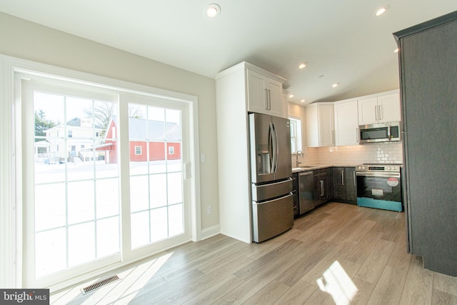 kitchen featuring tasteful backsplash, stainless steel appliances, vaulted ceiling, sink, and white cabinets