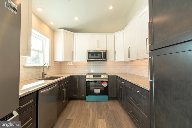 kitchen featuring sink, stainless steel appliances, backsplash, white cabinets, and light wood-type flooring