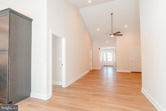 corridor with light wood-type flooring and high vaulted ceiling