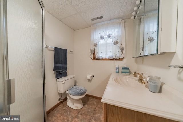 bathroom with toilet, tile patterned flooring, walk in shower, a drop ceiling, and vanity