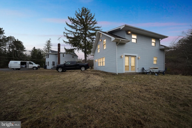 property exterior at dusk featuring french doors and a yard