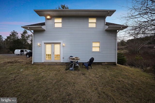 back house at dusk featuring french doors and a yard