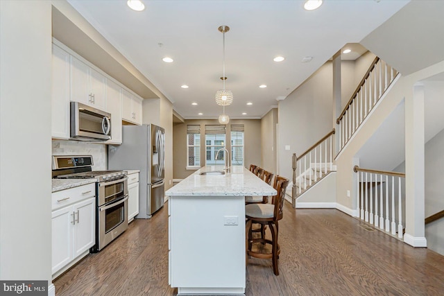 kitchen featuring appliances with stainless steel finishes, pendant lighting, sink, a kitchen island with sink, and light stone countertops