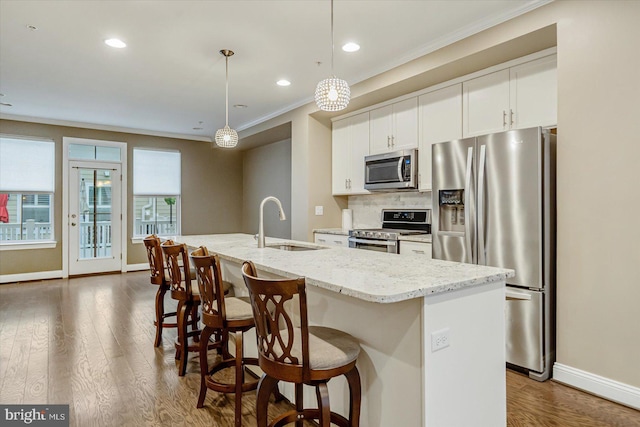 kitchen featuring white cabinetry, stainless steel appliances, a kitchen island with sink, and hanging light fixtures