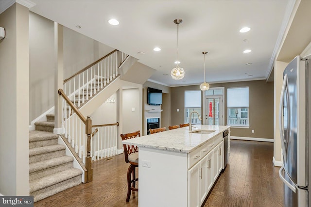 kitchen with decorative light fixtures, white cabinetry, sink, stainless steel appliances, and a center island with sink