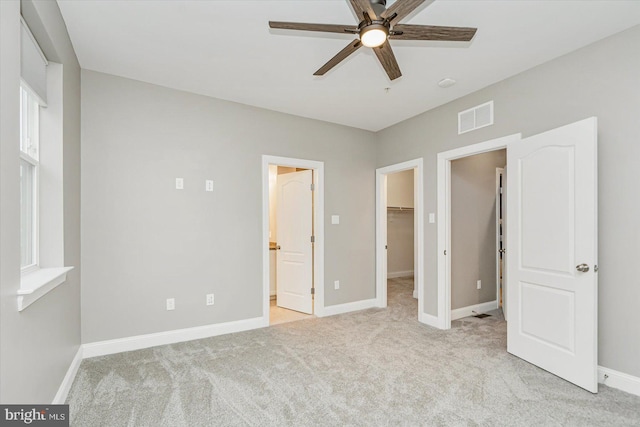 unfurnished bedroom with a spacious closet, light colored carpet, ceiling fan, ensuite bath, and a closet