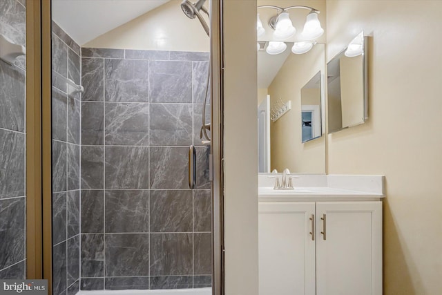 bathroom with a tile shower, vanity, and lofted ceiling