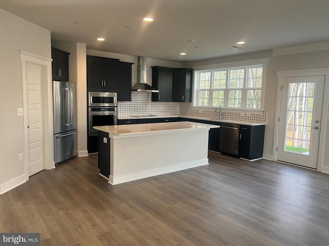 kitchen featuring backsplash, stainless steel appliances, dark wood-type flooring, wall chimney range hood, and a center island