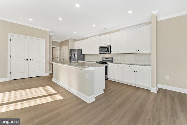 kitchen with white cabinetry, backsplash, stainless steel appliances, light stone counters, and a center island with sink