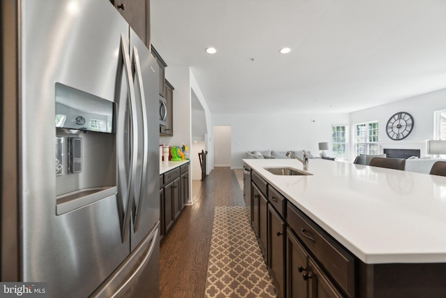 kitchen with dark hardwood / wood-style flooring, dark brown cabinets, sink, stainless steel fridge with ice dispenser, and an island with sink