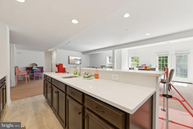 kitchen with a kitchen breakfast bar, dark brown cabinets, light colored carpet, a kitchen island with sink, and sink