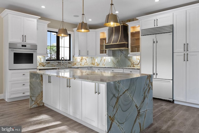 kitchen with a center island, light stone counters, appliances with stainless steel finishes, white cabinets, and custom exhaust hood