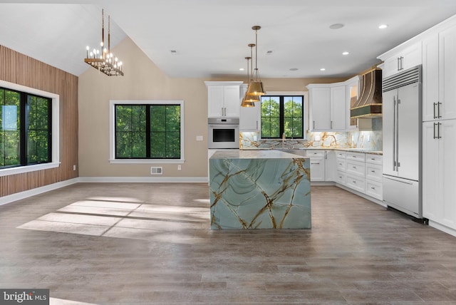 kitchen with pendant lighting, wall chimney exhaust hood, white cabinets, and appliances with stainless steel finishes