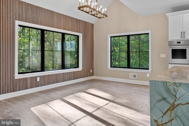 unfurnished dining area with a notable chandelier, wood walls, and lofted ceiling