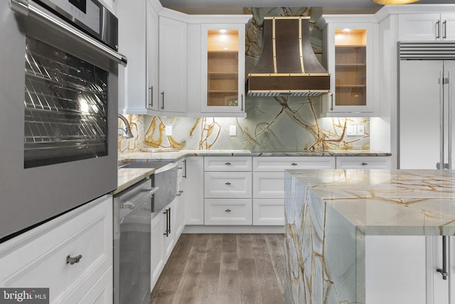 kitchen with tasteful backsplash, light stone countertops, white cabinets, and custom range hood