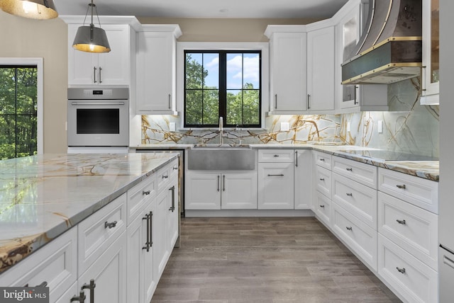 kitchen with pendant lighting, white cabinets, oven, black electric cooktop, and custom range hood