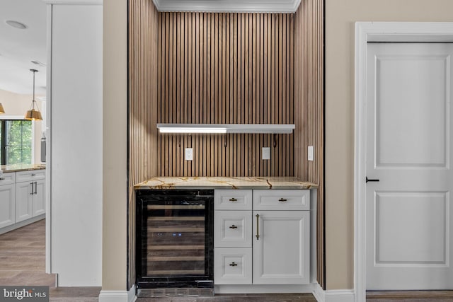 bar featuring light stone countertops, white cabinetry, beverage cooler, pendant lighting, and ornamental molding