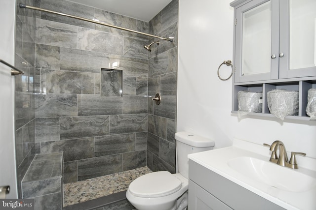 bathroom with a tile shower, vanity, and toilet