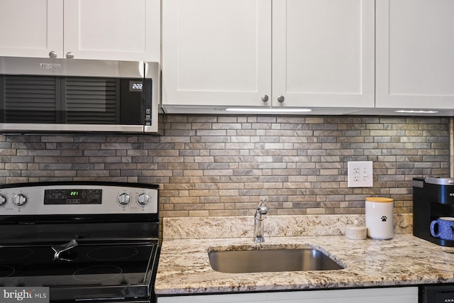 kitchen with backsplash, white cabinetry, sink, and range