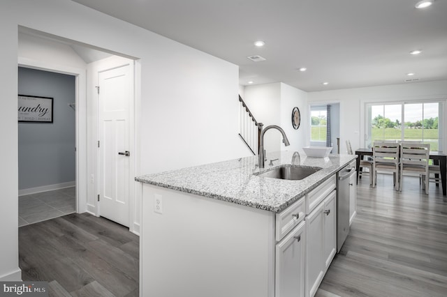 kitchen with a center island with sink, stainless steel dishwasher, sink, light stone countertops, and white cabinets