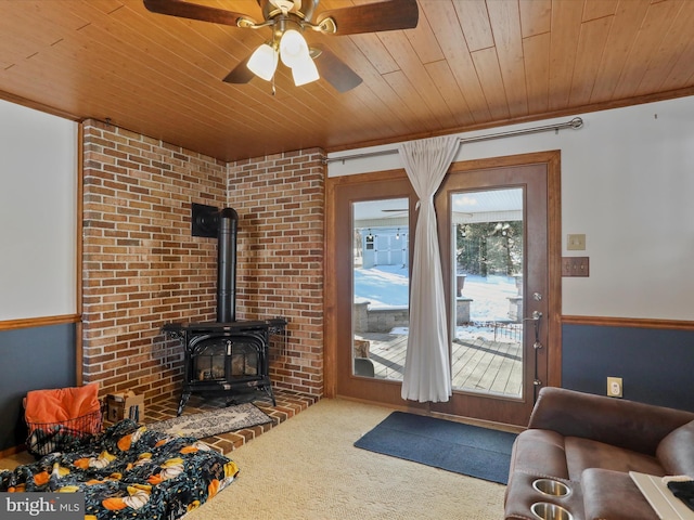 carpeted living room with ceiling fan, a wood stove, ornamental molding, and wooden ceiling