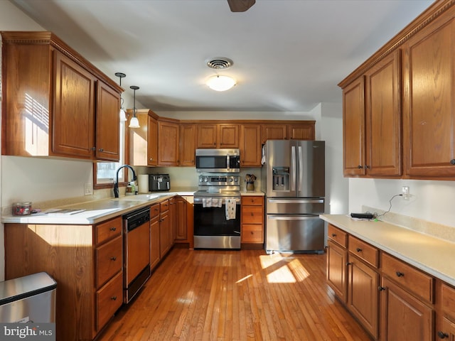 kitchen featuring decorative light fixtures, light wood-type flooring, sink, and appliances with stainless steel finishes