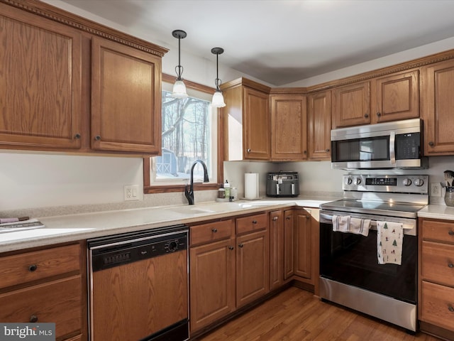 kitchen featuring pendant lighting, light hardwood / wood-style flooring, stainless steel appliances, and sink