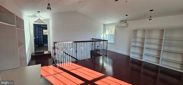 hallway with an AC wall unit, built in features, dark wood-type flooring, and vaulted ceiling