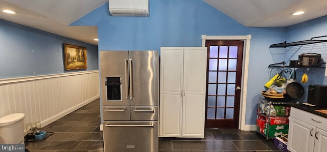 kitchen featuring a wall mounted air conditioner, high end refrigerator, lofted ceiling, wooden walls, and white cabinets