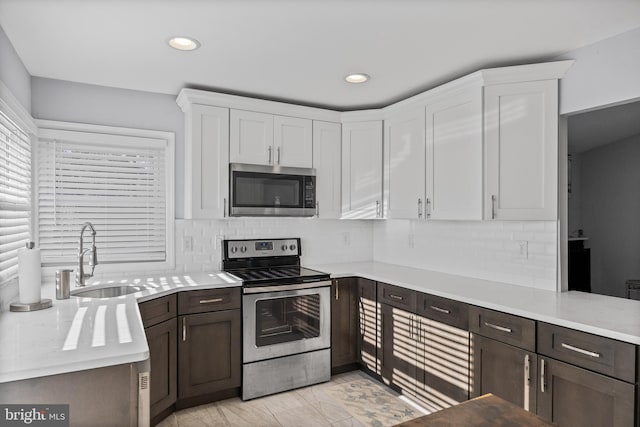 kitchen with appliances with stainless steel finishes, backsplash, dark brown cabinetry, sink, and white cabinetry