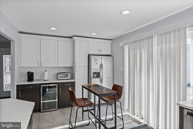 kitchen with stainless steel fridge, white cabinetry, backsplash, and beverage cooler