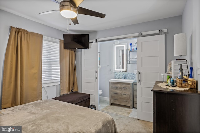 bedroom featuring a barn door, ceiling fan, and connected bathroom