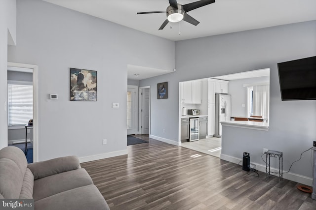 living room with ceiling fan, a towering ceiling, beverage cooler, and hardwood / wood-style flooring