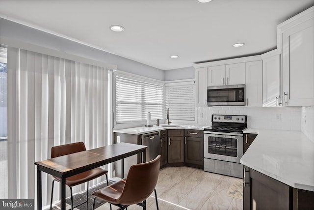 kitchen with appliances with stainless steel finishes, backsplash, dark brown cabinetry, sink, and white cabinetry