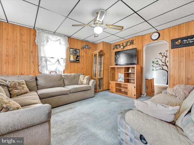 carpeted living room featuring a paneled ceiling, ceiling fan, and wooden walls