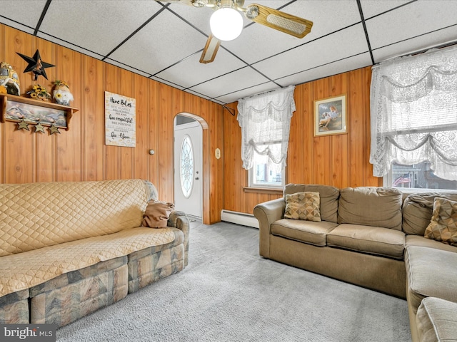 carpeted living room with a paneled ceiling, ceiling fan, wood walls, and baseboard heating