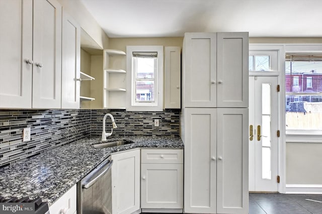 kitchen with stainless steel dishwasher, white cabinetry, sink, and dark stone counters