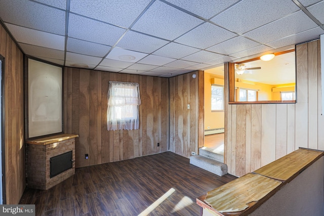 interior space with wooden walls, a baseboard heating unit, ceiling fan, and dark wood-type flooring