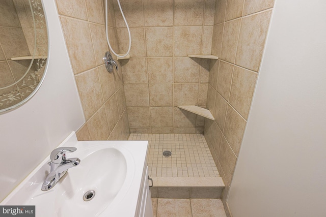 bathroom with tile patterned flooring, a tile shower, and vanity