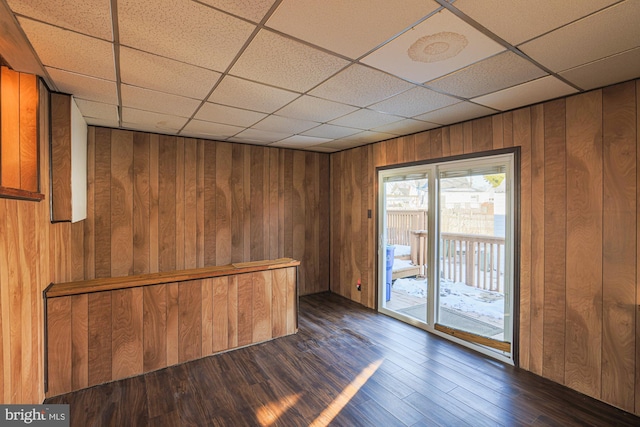 unfurnished room with a paneled ceiling, wooden walls, and dark hardwood / wood-style floors