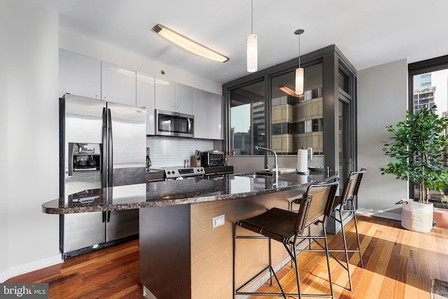 kitchen featuring stainless steel appliances, dark hardwood / wood-style flooring, backsplash, decorative light fixtures, and a breakfast bar