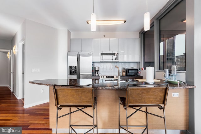 kitchen with a kitchen breakfast bar, dark stone counters, stainless steel appliances, and decorative light fixtures