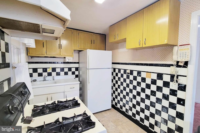 kitchen featuring white appliances, range hood, and sink