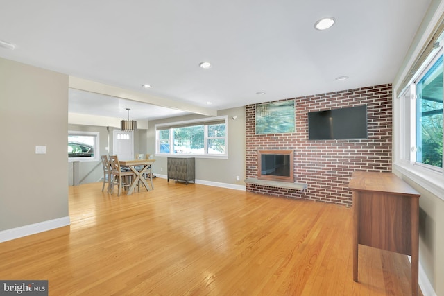 unfurnished living room with light hardwood / wood-style floors, brick wall, and a brick fireplace