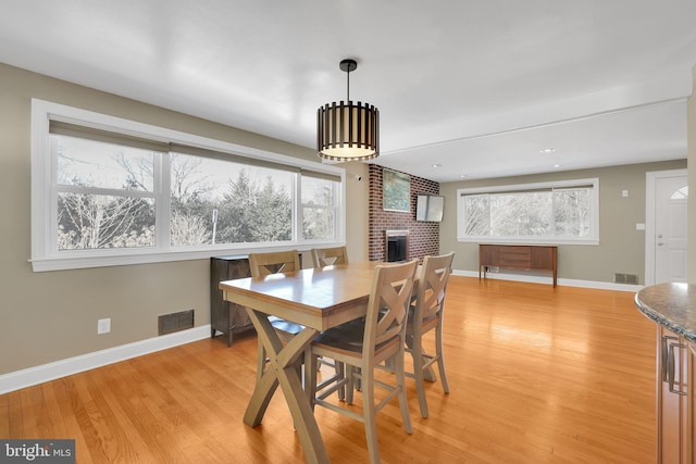 dining area with light wood-type flooring and a brick fireplace