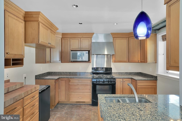 kitchen with gas stove, sink, wall chimney exhaust hood, hanging light fixtures, and dark stone counters