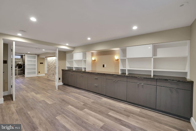 kitchen featuring built in shelves, light hardwood / wood-style flooring, washer / clothes dryer, dark stone counters, and dark brown cabinets