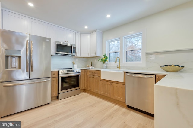 kitchen with sink, light hardwood / wood-style flooring, appliances with stainless steel finishes, tasteful backsplash, and white cabinetry