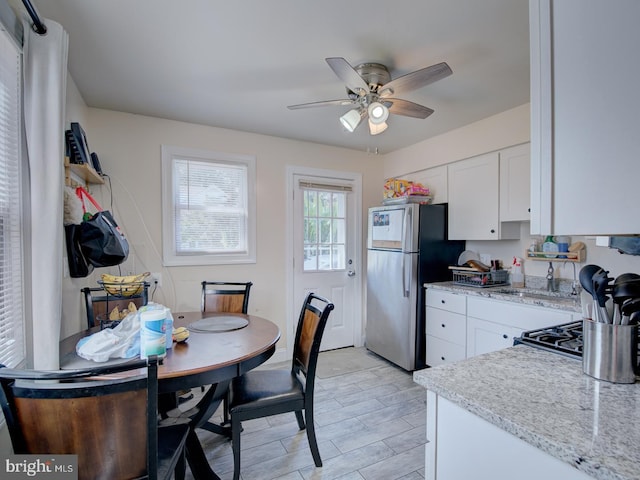 kitchen with white cabinets, stainless steel refrigerator, ceiling fan, and light stone counters